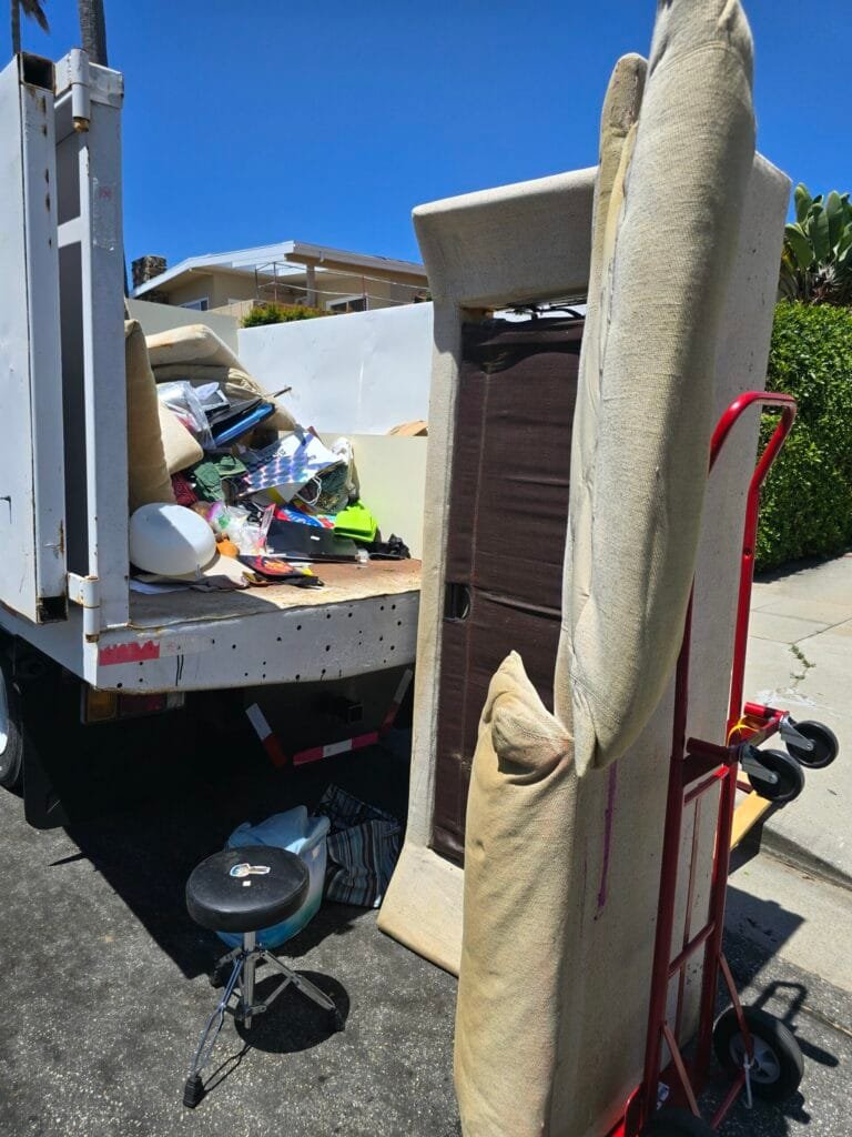Box truck parked at the curb with a hand truck and a mattress ready to load