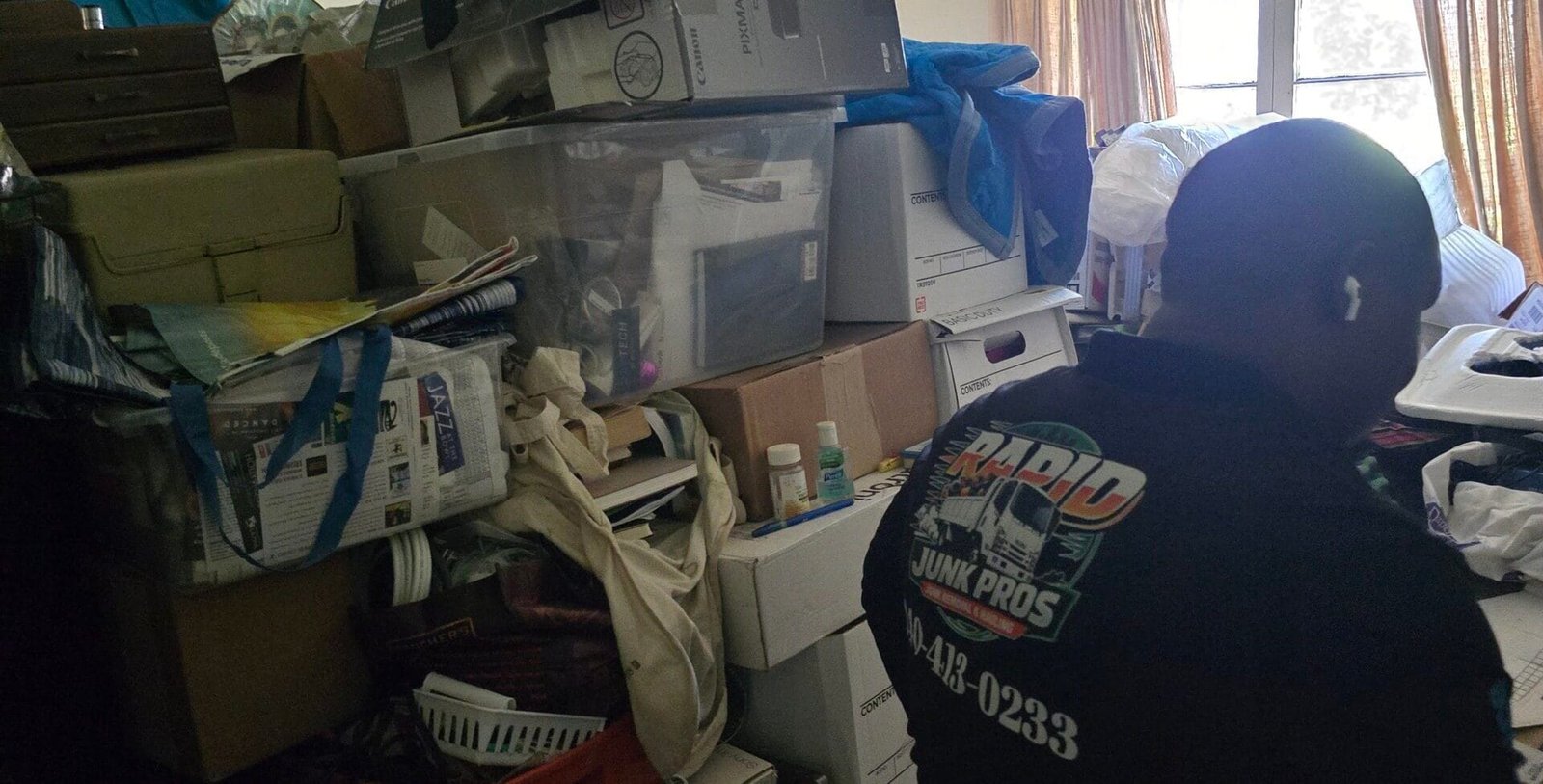 Rapid Junk Pros crew member standing among stacked boxes in a crowded room